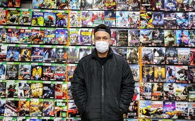 Un vendeur portant un masque se tient devant des titres de jeux vidéo sur un mur, dans un magasin de jeux et de consoles sur le marché central de la capitale iranienne, Téhéran, le 24 janvier 2021. (Crédit : ATTA KENARE / AFP) Un vendeur portant un masque se tient devant des titres de jeux vidéo sur un mur, dans un magasin de jeux et de consoles sur le marché central de la capitale iranienne, Téhéran, le 24 janvier 2021. (Crédit : ATTA KENARE / AFP)