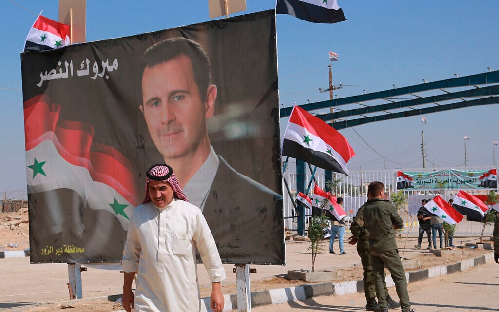 Illustration : Un homme passant devant une affiche présentant le dictateur syrien Bashar el-Assad en franchissant la frontière, au point de passage situé entre la ville de Qaim (Irak) et Boukamal (Syrie), le 30 septembre 2019. (Crédit : Hadi Mizban/AP Photo/Dossier) Illustration : Un homme passant devant une affiche présentant le dictateur syrien Bashar el-Assad en franchissant la frontière, au point de passage situé entre la ville de Qaim (Irak) et Boukamal (Syrie), le 30 septembre 2019. (Crédit : Hadi Mizban/AP Photo/Dossier)