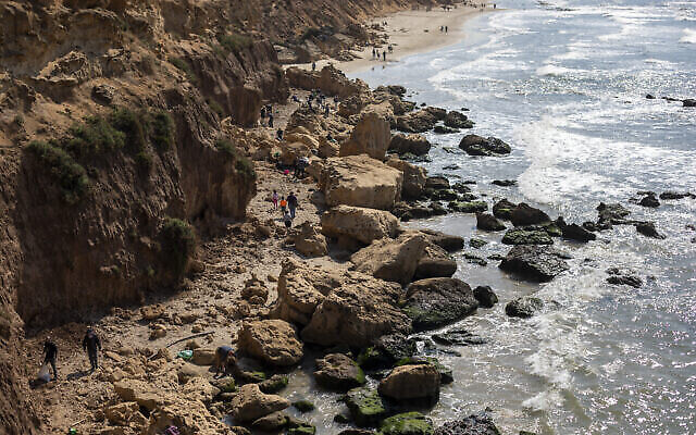 Des Israéliens nettoient du goudron provenant d'une fuite de pétrole dans la mer méditerranée dans la réserve naturelle de Gador, près de Hadera, le 20 février 2021. (Crédit : AP Photo/Ariel Schalit)