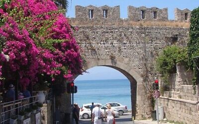 Des touristes se promenant le long des vieux murs de la ville de Rhodes, près de la place des Martyrs juifs. (Crédit : Gavin Rabinowitz/JTA)