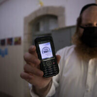 Un enseignant montrant son téléphone portable certifiant qu'il est "casher", à l'entrée d'une école ultra-orthodoxe, à Jérusalem, le 6 mai 2020. (Crédit : Nati Shohat/Flash90)