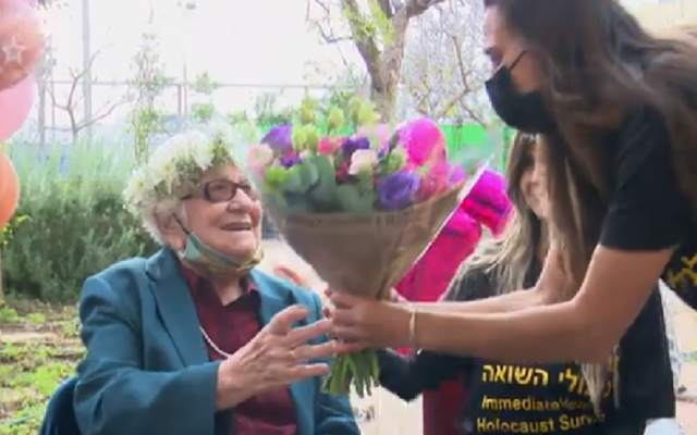 Un bénévole de l'Association d'aide immédiate aux survivants de la Shoah offre des fleurs à Frieda Kliger pour son 100e anniversaire, le 14 mars 2021. (Capture d'écran Douzième chaîne) Un bénévole de l'Association d'aide immédiate aux survivants de la Shoah offre des fleurs à Frieda Kliger pour son 100e anniversaire, le 14 mars 2021. (Capture d'écran Douzième chaîne)
