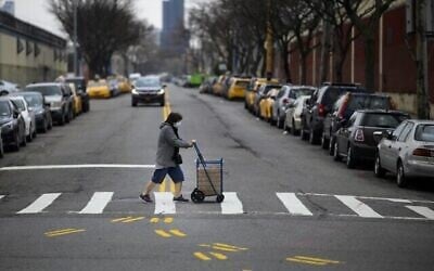 Une femme portant un masque pousse un caddie en traversant une rue du Queens, le 30 mars 2019 à New York. (Johannes EISELE / AFP)