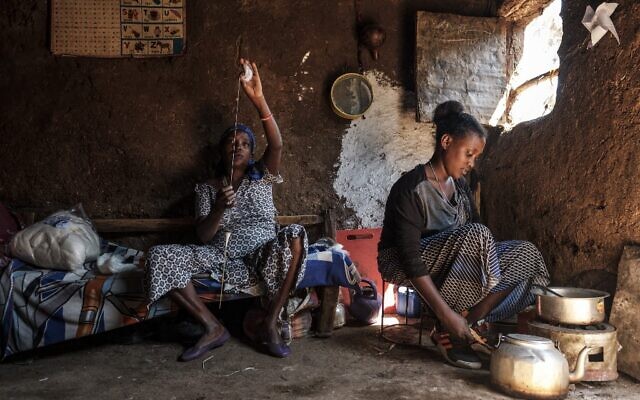 Une femme membre de la communauté juive éthiopienne tricote tandis qu'une autre cuisine, dans la ville de Gondar, en Ethiopie, le 27 octobre 2020. (Crédit : EDUARDO SOTERAS / AFP)
