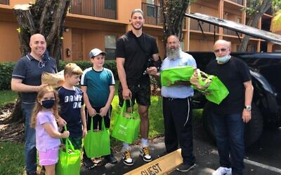 Meyers Leonard, au centre, distribue des repas de Pessah à des survivants de la Shoah et des seniors juifs dans la région de Miami avec l'aide du rabbin Pinny Andrusier, à sa gauche. (Crédit : Chabad of Southwest Broward via JTA)