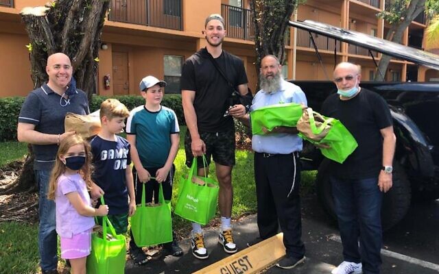 Meyers Leonard, au centre, distribue des repas de Pessah à des survivants de la Shoah et des seniors juifs dans la région de Miami avec l'aide du rabbin Pinny Andrusier, à sa gauche. (Crédit : Chabad of Southwest Broward via JTA)