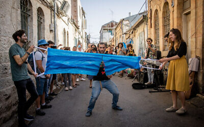 Un Israélien coupe un masque géant pour fêter la fin de l'obligation du port du masque à Jérusalem, le 18 avril 2021. (Crédit :  Yonatan Sindel/Flash90)