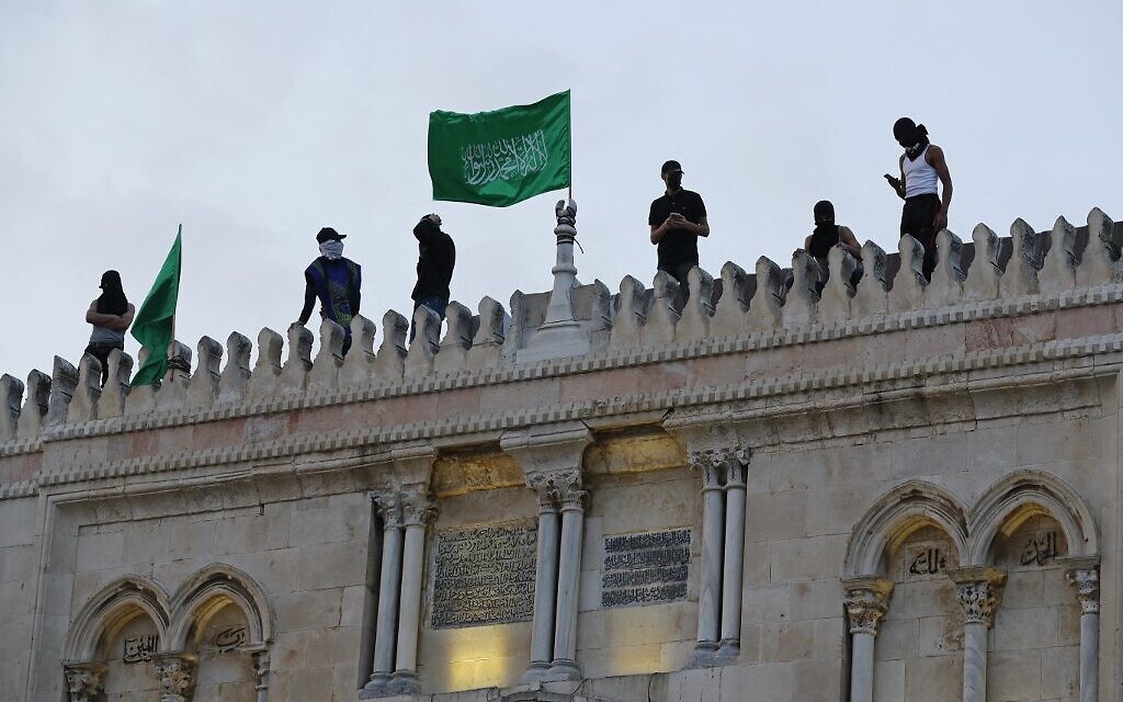 Des Palestiniens placent les drapeaux du Hamas au sommet de la mosquée al-Aqsa dans la vieille ville de Jérusalem, le 10 mai 2021, avant une marche prévue pour commémorer la prise de Jérusalem par Israël lors de la guerre des Six Jours en 1967. (Crédit : Ahmad GHARABLI / AFP)
