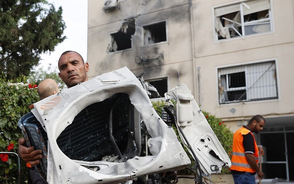 Un homme montre des morceaux d'une voiture touchée par une roquette lancée depuis Gaza à Ashkelon, le 11 mai 2021. (Crédit :  JACK GUEZ / AFP)
