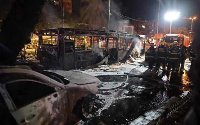 Des pompiers israéliens près d'un bus et d'autres véhicules touchés par un tir de roquette de Gaza à Holon près de Tel Aviv, le 11 mai 2021. (Ahmad Gharabli / AFP)