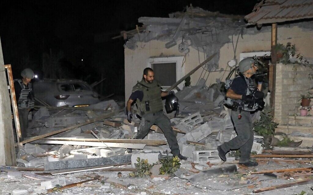 Des pompiers et des forces de sécurité israéliens inspectent les dégâts d'une maison touchée par une roquette tirée depuis Gaza, le 12 mai 2021 (Crédit : GIL COHEN-MAGEN / AFP)