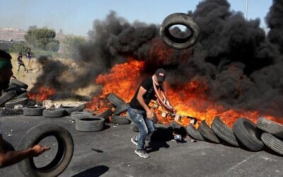 Un émeutier palestinien jette un pneu en feu sur un tas lors d'affrontements avec l'armée israélienne près de l'implantation juive de Beit El à proximité de Ramallah en Cisjordanie, le 14 mai 2021 (Crédit : ABBAS MOMANI / AFP)