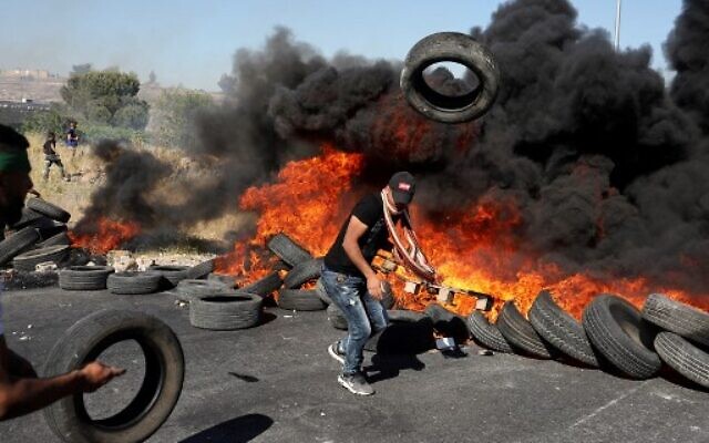 Un émeutier palestinien jette un pneu en feu sur un tas lors d'affrontements avec l'armée israélienne près de l'implantation juive de Beit El à proximité de Ramallah en Cisjordanie, le 14 mai 2021 (Crédit : ABBAS MOMANI / AFP) Un émeutier palestinien jette un pneu en feu sur un tas lors d'affrontements avec l'armée israélienne près de l'implantation juive de Beit El à proximité de Ramallah en Cisjordanie, le 14 mai 2021 (Crédit : ABBAS MOMANI / AFP)