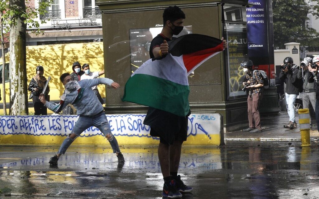 Un manifestant tient un drapeau palestinien devant des policiers français alors qu'un autre tire un projectile sur les forces de l'ordre, à Paris, le 15 mai 2021. (Crédit : GEOFFROY VAN DER HASSELT / AFP)