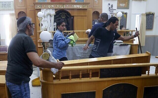 Des fidèles nettoient l'intérieur d'une synagogue endommagée suite à un tir de roquette de Gaza à Ashkelon, le 16 mai 2021. (Crédit : Jack Guez/AFP)