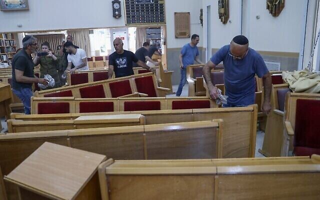 Des fidèles nettoient l'intérieur d'une synagogue endommagée suite à un tir de roquette de Gaza à Ashkelon, le 16 mai 2021. (Crédit : Jack Guez/AFP)