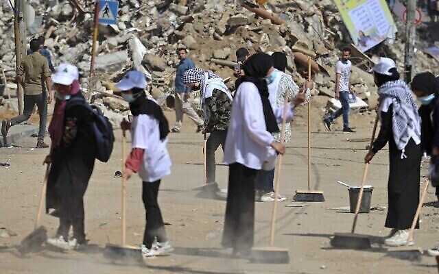 Des volontaires palestiniens balaient la poussière devant un bâtiment détruit lors de la dernière série de combats, dans le quartier Rimal de la ville de Gaza, le 25 mai 2021. (Crédit : MOHAMMED ABED / AFP)
