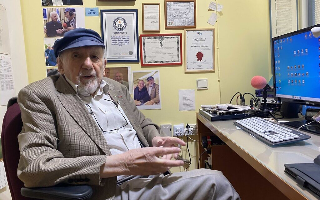 Le journaliste de radio Walter Bingham assis à son bureau de Jérusalem, de multiples souvenirs accrochés au mur, notamment un télégramme concernant une récompense donnée par le roi britannique George VI. (Sam Sokol/ JTA)