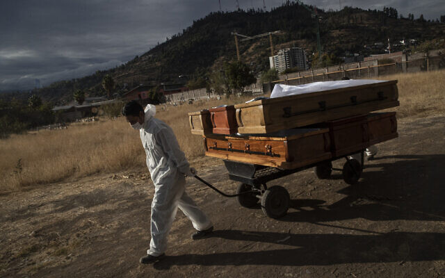Un employé des pompes funèbres tire des cercueils vides qui transportaient des corps qui ont été incinérés au cimetière La Recoleta  à Santiago, au Chili, dans le cadre de la pandémie de coronavirus, le 21 avril 2021. (Crédit : AP Photo/Esteban Felix)