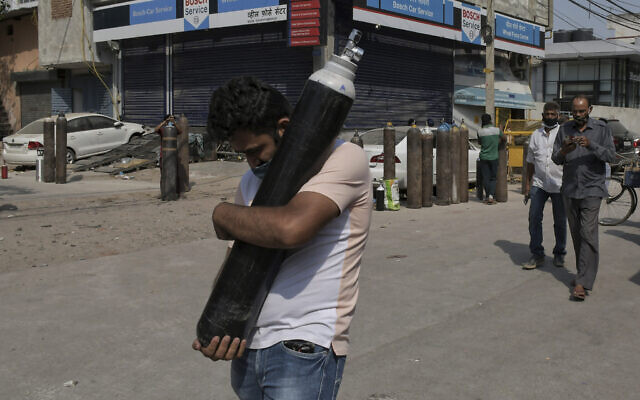 Un homme marche en portant une bonbonne d'oxygène remplie pendant que les membres de la famille des patients du COVID-19 font la queue pour remplir leur bouteille d'oxygène dans le quartier de Mayapuri à New Delhi, en Inde, le 3 mai 2021. (Crédiy : Ishant Chauhan/AP) Un homme marche en portant une bonbonne d'oxygène remplie pendant que les membres de la famille des patients du COVID-19 font la queue pour remplir leur bouteille d'oxygène dans le quartier de Mayapuri à New Delhi, en Inde, le 3 mai 2021. (Crédiy : Ishant Chauhan/AP)