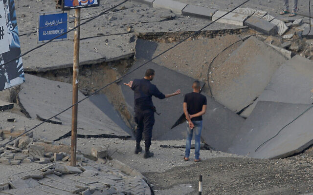 Des personnes se tiennent dans une rue détruite par une frappe aérienne israélienne dans la ville de Gaza en réponse à un tir de roquette, le 13 mai 2021 (Crédit : AP Photo/Hatem Moussa).