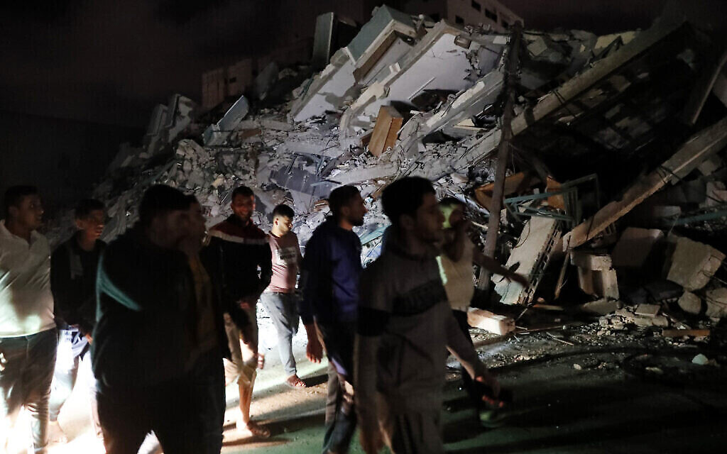 Des Palestiniens célèbrent l'accord de cessez-le-feu entre Israël et le Hamas en passant devant les décombres d'un bâtiment détruit dans la ville de Gaza, le 21 mai 2021. (Crédit : AP Photo/Adel Hana)