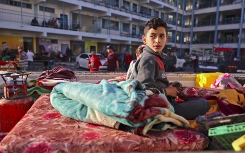Un garçon palestinien qui a fui son domicile en raison des frappes aériennes israéliennes, menées en guise de représailles aux pluies de roquettes des groupes terroristes palestinien de Gaza visant Israël, est assis sur un matelas devant une école accueillant des réfugiés dans la ville de Gaza, le 14 mai 2021 (Crédit : MOHAMMED ABED / AFP)