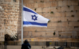Les gens marchent à côté d'un drapeau israélien en l'honneur des victimes du mont Meron, victimes de la catastrophe, au mur Occidental dans la Vieille Ville de Jérusalem, le 2 mai 2021 (Crédit : Yonatan Sindel / Flash90)