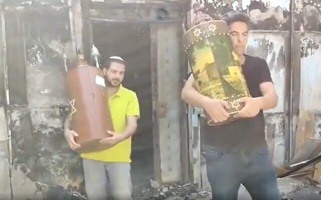 Des habitants de Lod récupèrent des rouleaux de la Torah indemnes dans les ruines d'une synagogue incendiée par des émeutiers arabes, le 12 mai 2021. (Capture d'écran : Twitter)
