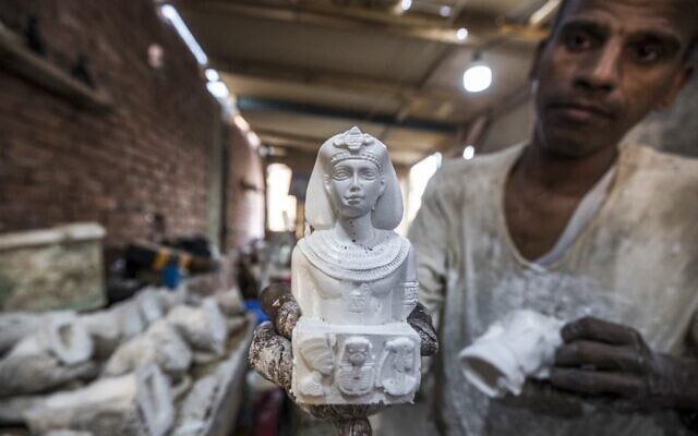 Un artisan manipule une réplique moulée d'une figurine de buste de l'ancienne Égypte dans un atelier du quartier de Nazlet el-Semman, près de la nécropole des pyramides de Gizeh, dans la ville jumelle de la capitale égyptienne, Gizeh, le 6 juin 2021. (Crédit : Khaled DESOUKI / AFP)