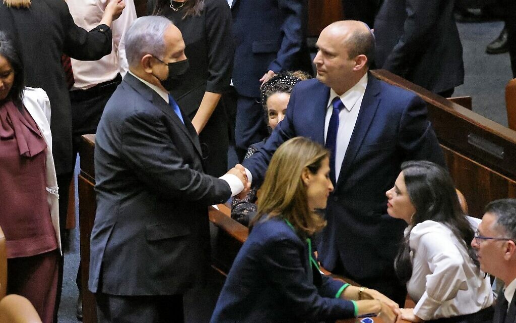 De gauche à droite : Le Premier ministre israélien sortant Benjamin Netanyahu serre la main à son successeur, le prochain Premier ministre Naftali Bennett, après une session spéciale de vote du nouveau gouvernement à la Knesset de Jérusalem, le 13 juin 2021. (Crédit :  EMMANUEL DUNAND / AFP)