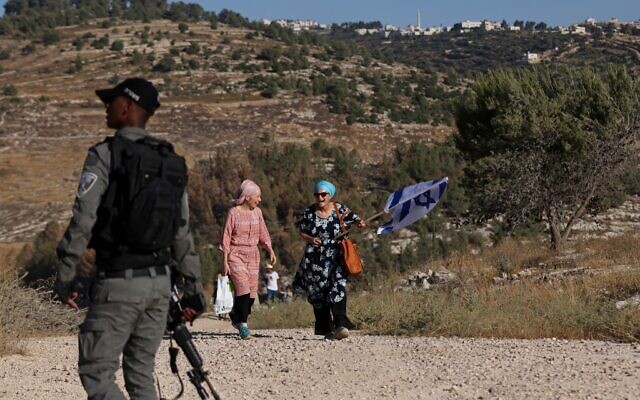 Des partisans du mouvement pro-implantation défilent avec un drapeau israélien sur une colline à proximité de l'implantation de Bat Ayin en Cisjordanie, le 21 juin 2021. (Crédit : Emmanuel DUNAND / AFP) Des partisans du mouvement pro-implantation défilent avec un drapeau israélien sur une colline à proximité de l'implantation de Bat Ayin en Cisjordanie, le 21 juin 2021. (Crédit : Emmanuel DUNAND / AFP)
