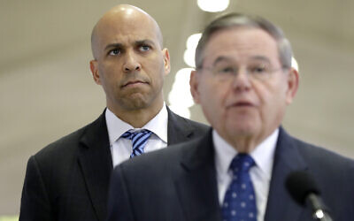 Le sénateur américain Cory Booker, en arrière plan, regarde le sénateur Bob Menendez prendre la parole lors d'une conférence de presse à l'aéroport international Newark Liberty, le 8 janvier 2019, à Newark, N.J. (Crédit : AP Photo/Julio Cortez)