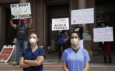 Des personnels de santé portant une blouse et un masque regardent une manifestation "Open Texas" , état soumis au confinement en raison de la COVID-19, au Capitole de l'état du Texas, le 25 avril 2020. (Crédit : AP Photo/Eric Gay)