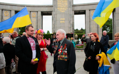 David Dushman, dernier libérateur encore en vie du camp de concentration nazi d'Auschwitz et un escrimeur de talent, ici à 92 ans, au centre, s'entretient avec des personnes tenant des drapeaux ukrainiens alors qu'il assiste à une cérémonie de dépôt de couronnes de fleurs au Mémorial de la guerre russe dans le quartier Tiergarten de Berlin, en Allemagne, le 8 mai 2015. (Crédit : AP Photo/Markus Schreiber)