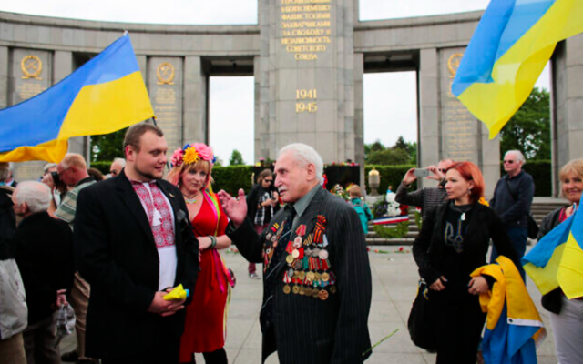David Dushman, dernier libérateur encore en vie du camp de concentration nazi d'Auschwitz et un escrimeur de talent, ici à 92 ans, au centre, s'entretient avec des personnes tenant des drapeaux ukrainiens alors qu'il assiste à une cérémonie de dépôt de couronnes de fleurs au Mémorial de la guerre russe dans le quartier Tiergarten de Berlin, en Allemagne, le 8 mai 2015. (Crédit : AP Photo/Markus Schreiber)