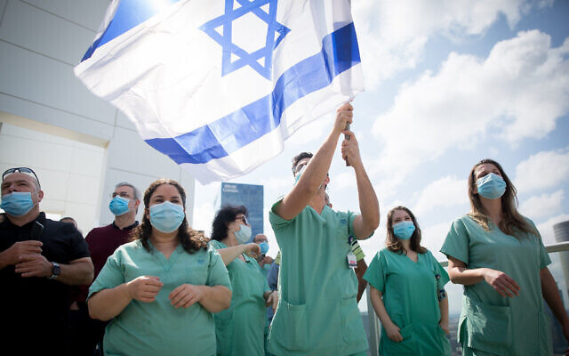 Le personnel médical israélien applaudit une équipe acrobatique de Tsahal qui survole l'hôpital Ichilov à Tel-Aviv lors du 72e jour de l'indépendance d'Israël, le 29 avril 2020 (Crédit : Miriam Alster/Flash90).