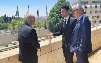 Le ministre des Affaires étrangères Yair Lapid, le vice-ministre des Affaires étrangères Idan Roll et le directeur général du ministère des Affaires étrangères Alon Ushpiz, à côté du drapeau LGBT installé le 21 juin 2021. (Crédit : Ministère des affaires étrangères)