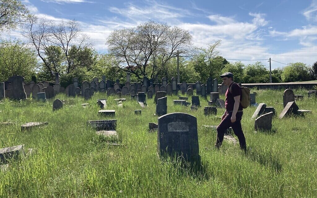 Matyas Kiraly marche parmi des pierres tombales renversées et vandalisées dans l'ancien cimetière juif de Nagyteteny, le 11 mai 2021. (Crédit: Yaakov Schwartz/ Times of Israel)