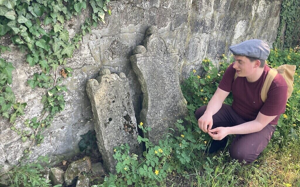 Matyas Kiraly s'agenouille à côté de certaines des pierres tombales les plus anciennes, datant de 1750, dans l'ancien cimetière juif de Nagyteteny, le 11 mai 2021. (Crédit : Yaakov Schwartz/ Times of Israel)