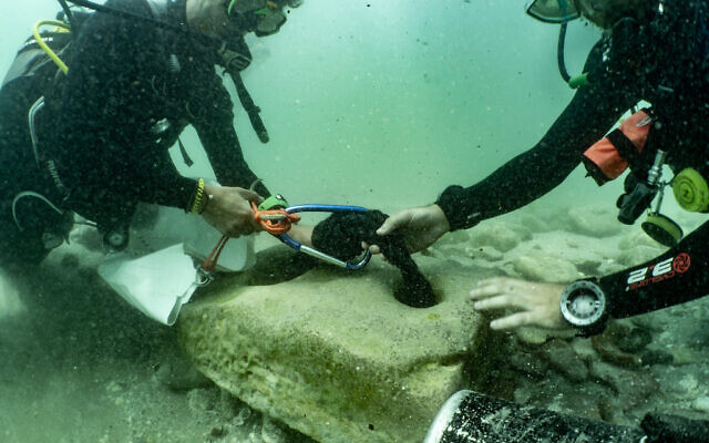 Des plongeurs, avec une ancienne ancre en pierre qui a été retrouvée sur le site archéologique de Tel Dor, dans le nord d'Israël, le 10 juin 2021. (Crédit : Amir Yurman de l'atelier maritime de l'Université de Haïfa) Des plongeurs, avec une ancienne ancre en pierre qui a été retrouvée sur le site archéologique de Tel Dor, dans le nord d'Israël, le 10 juin 2021. (Crédit : Amir Yurman de l'atelier maritime de l'Université de Haïfa)