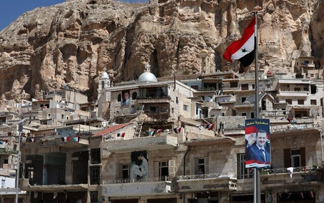 Un drapeau national et des portraits du président syrien Bashar al-Assad dans le village de Maalula, au nord Damas, le 29 juin 2021. (Crédit : LOUAI BESHARA / AFP)