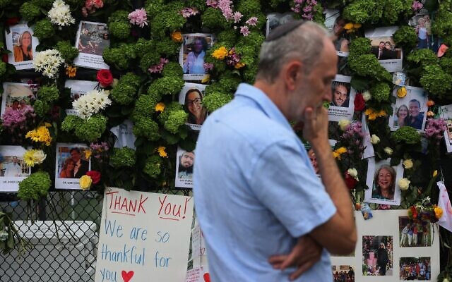 Un homme passe devant un mémorial où figurent les photos de certains des disparus de l'immeuble de 12 étages Champlain Towers South, à Surfside, en Floride, qui s'est partiellement effondré, le 28 juin 2021. (Crédit : Joe Raedle/Getty Images/AFP)