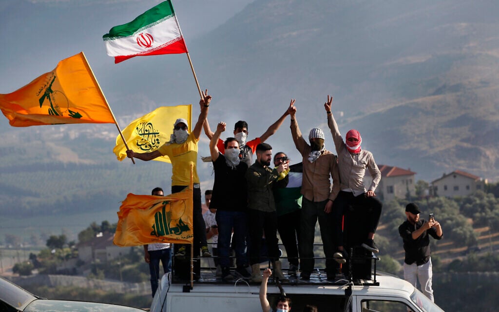Des partisans du Hezbollah brandissent les drapeaux Palestinien, Iranien et du groupe terroriste libanais lors d'une manifestation à la frontière dans le cadre de la campagne militaire menée par les Israéliens à Gaza, à la frontière entre Israël et le Liban, devant l'implantation de Metula, en arrière-plan, le 14 mai 2021. (Crédit : AP Photo/Mohammed Zaatari)