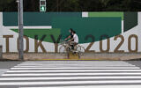 Des hommes font du vélo le long du mur installé pour fermer un parc en préparation pour les Jeux olympiques et paralympiques à Tokyo, le 1er juillet 2021. (Crédit : AP Photo/Hiro Komae)