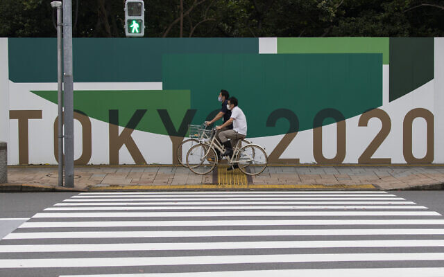 Des hommes font du vélo le long du mur installé pour fermer un parc en préparation pour les Jeux olympiques et paralympiques à Tokyo, le 1er juillet 2021. (Crédit : AP Photo/Hiro Komae) Des hommes font du vélo le long du mur installé pour fermer un parc en préparation pour les Jeux olympiques et paralympiques à Tokyo, le 1er juillet 2021. (Crédit : AP Photo/Hiro Komae)