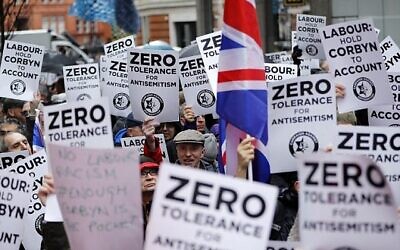 Illustration : Des personnes brandissent des pancartes et des drapeaux de l'Union alors qu'elles se rassemblent pour une manifestation organisée par la Campagne contre l'antisémitisme devant le siège du Parti travailliste, l'opposition britannique, dans le centre de Londres, le 8 avril 2018. (Crédit : AFP/Tolga Akmen)
