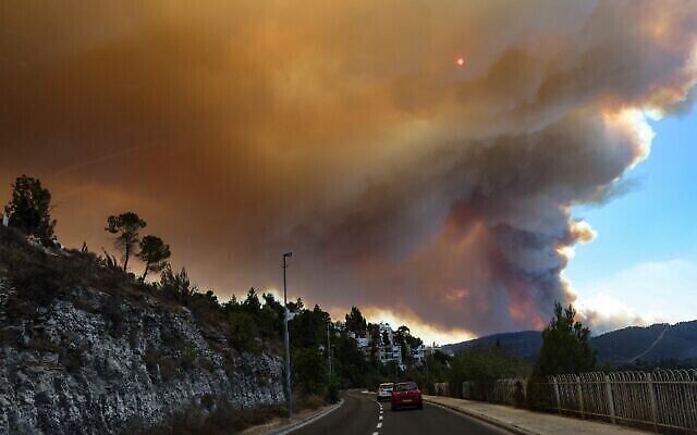 Des voitures circulent alors que des flammes et de la fumée s'élèvent suite à un feu de forêt sur les montagnes de Jérusalem, près du village du Moshav Shoresh, le 15 août 2021. (Crédit :Menahem KAHANA / AFP)