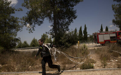 Un pompier israélien court avec des tuyaux tout en combattant des incendies de forêt près de Shoresh, à la périphérie de Jérusalem, le 16 août 2021. (Crédit : AP Photo/Maya Alleruzzo)