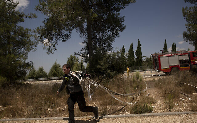 Un pompier israélien court avec des tuyaux tout en combattant des incendies de forêt près de Shoresh, à la périphérie de Jérusalem, le 16 août 2021. (Crédit : AP Photo/Maya Alleruzzo)